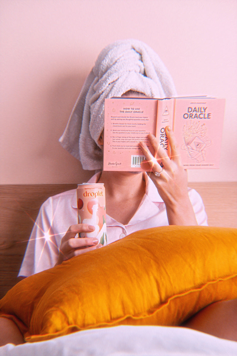 woman in her pajamas in bed with a spiritual book in one hand, and pretty balanced in the other.